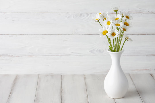 Chamomiles or daisies in white vase on wooden planks, summer flowers composition
