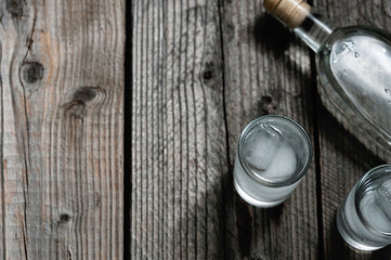 Two shot glasses with cold vodka or gin on wooden table,