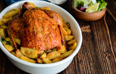 Roasted whole chicken with potatoes and thyme in a white dish.