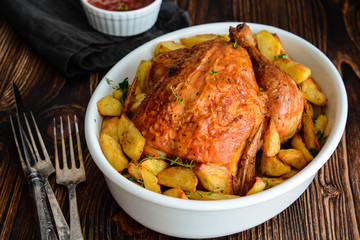 Roasted whole chicken with potatoes and thyme in a white dish.