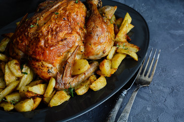 Roasted chicken and potatoes on black slate stone background, flat lay with copy space. 