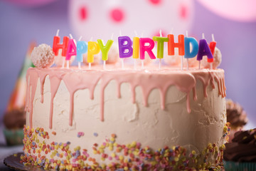 happy birthday candles on pink white birthday cake with coconut balls balloon background 