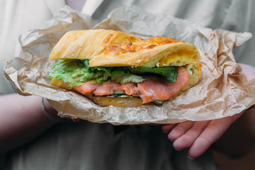 Sandwich with salmon on kraft paper in the hands of a woman