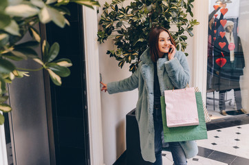 Smiling and happy female after shopping with bags pushing the button and call the elevator and speaking on phone