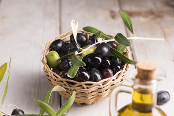 Olives and a bottle of olive oil on white dark wooden table