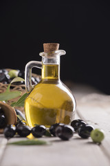 Olives and a bottle of olive oil on white dark wooden table