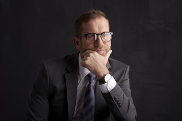 Thinking businessman portrait. Studio shot of wrinkled face business man wearing suit and looking thoughtful while sitting at dark background. Professional man wearing suit and tie. 