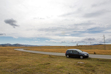 Plakat car with the traveler stands on the roadside in a yellow field in zabljak in Montenegro in autumn