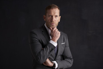 Fototapeta premium Thinking businessman portrait. Studio shot of wrinkled face business man wearing suit and looking thoughtful while sitting at dark background. Professional man wearing suit and tie. 
