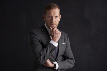 Nervous, overwhelmed businessman portrait.  Stressed businessman hand is on his forehead while sitting at dark background and thinking very hard. Professional man wearing suit.