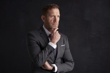 Nervous, overwhelmed businessman portrait.  Stressed businessman hand is on his forehead while sitting at dark background and thinking very hard. Professional man wearing suit.