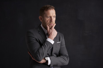 Nervous, overwhelmed businessman portrait.  Stressed businessman hand is on his forehead while sitting at dark background and thinking very hard. Professional man wearing suit.