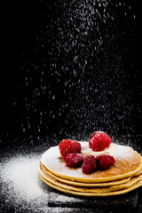 Pancakes with berries and sugar on dark background