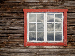 wooden houses with red windows and reflections from the clouds in the window