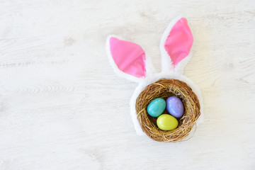 A nest with three colored Easter eggs and bunny ears at home on Easter day. Celebrating Easter at spring.