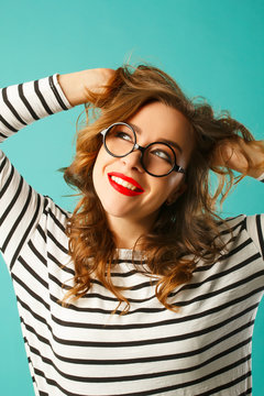 Funny pretty woman in round transparent glasses holding hands on her head over blue background