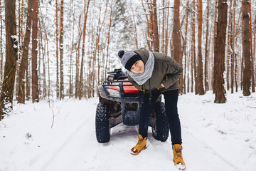 A boy is standing near a quad bike in the middle of the forest
