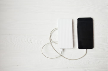 Smartphone with white powerbank on wood desk.