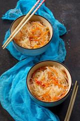 Funchoza salad with rice noodles with paprika, tomatoes and pepper on a dark stone or slate background.