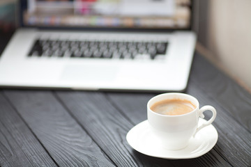 Coffee Cup on the white table on blurred laptop background for Business Concept.