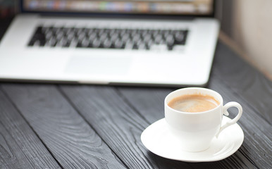 Coffee Cup on the white table on blurred laptop background for Business Concept.