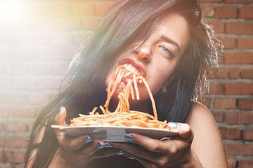 Sexy seductive girl in white T-shirt with plate of pasta and ketchup, without fork eats pasta....