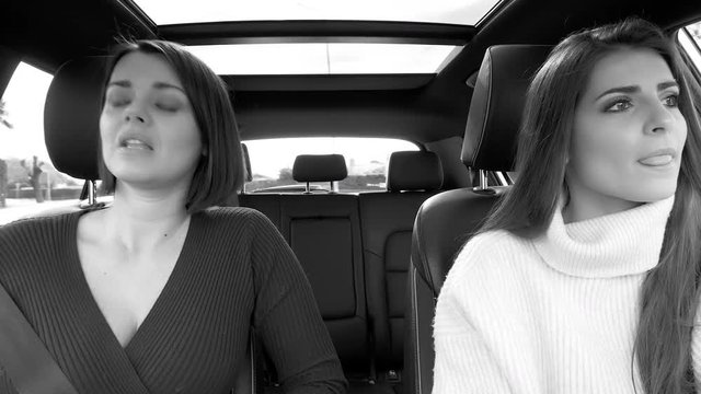 Two happy beautiful women driving car singing listening music black and white