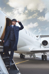 Low angle full length side view happy aviator situating near exit of airplane. Occupation concept