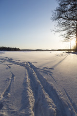 Wintry scenery in Finland. Very cold day in Finland, path and ski tracks in the snow. Sunset behind the lake, some flare added in the image. Deep snow.