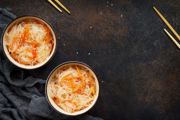 Funchoza salad with rice noodles with paprika and pepper on a dark stone or slate background, top view with copy space.