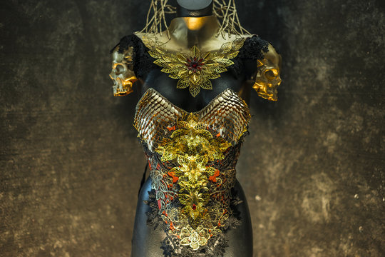 fantastic gold armor and handmade metal pieces, it has a gold dragon scaled breastplate with a helmet of gothic pieces and red feathers, it has a red skirt and metal pieces of jewelery