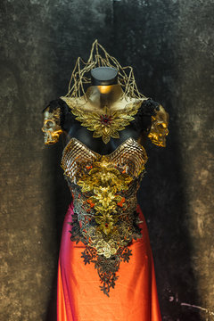 Medieval, fantastic gold armor and handmade metal pieces, it has a gold dragon scaled breastplate with a helmet of gothic pieces and red feathers, it has a red skirt and metal pieces of jewelery