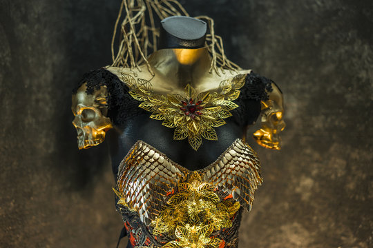 fantastic gold armor and handmade metal pieces, it has a gold dragon scaled breastplate with a helmet of gothic pieces and red feathers, it has a red skirt and metal pieces of jewelery