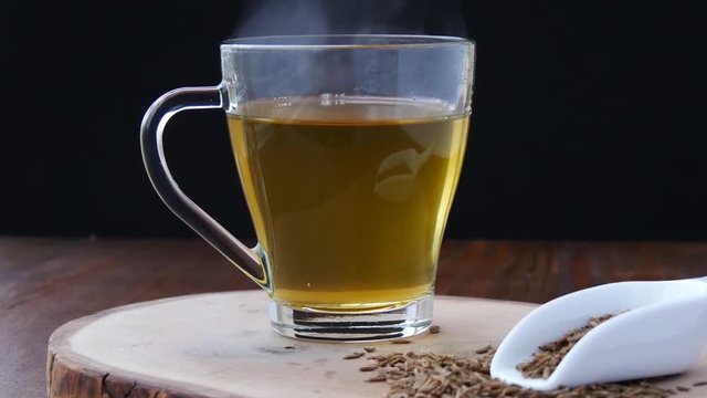 Steaming cumin seed tea with honey, jeera water for weight loss in glass mug closeup, vertical panning