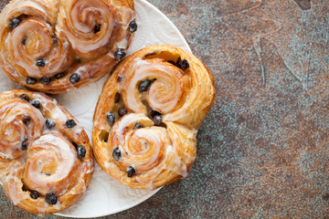 Fototapeta premium Fresh buns with raisins and icing on old rusty background. Top view with copy space