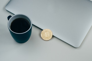 Bitcoin coin near grey laptop and blue coffee cup. Cryptocurrency concept. Isolated on white background