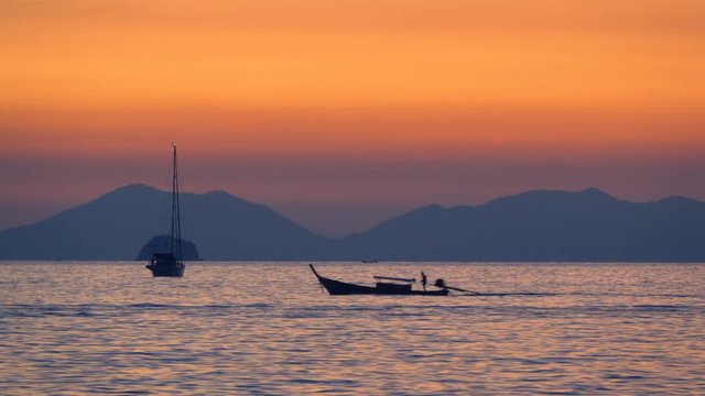 Mast yacht in Andaman sea with an Andaman islands on background and floating Thai long-tail boat in foreground at sunset 
