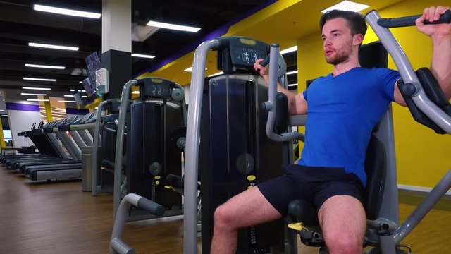 A young fit man trains on a machine in a gym