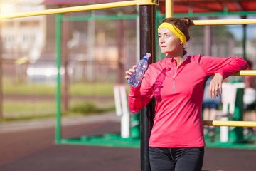 Sport, Fitness and Workout Concepts. Happy Smiling Caucasian Female Athlete in Professional Outfit Posing With Water Bottle Near the Trainer Outdoors.