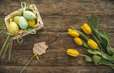 Top view of bouquet of flowers, colored eggs in the box and holiday felicitation