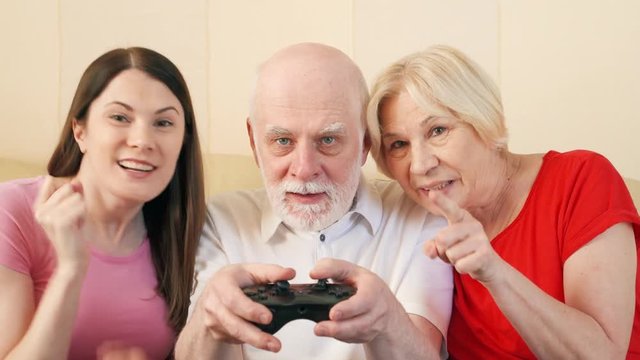 Senior couple and their teenage daughter gamers playing video game at home. Addicted seniors and teen players with remote controller of game console. Cybersport for active modern elderly people