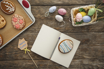 Top view close up of easter decorations and opened exercise book with pen and egg shaped cookie on it
