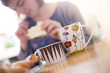 Junge Frau am Frühstückstisch, Teetasse im Vordergrund, Unschärfe