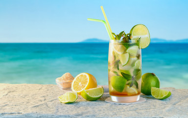 Mojito cocktail. White rum cocktail with fresh ingredients. Cold ice drink on blurred beach background.