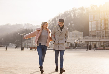 Fototapeta premium Walking together. Full length of happy young couple on date is having fun outdoors. They are going hand in hand while enjoying sunny spring day