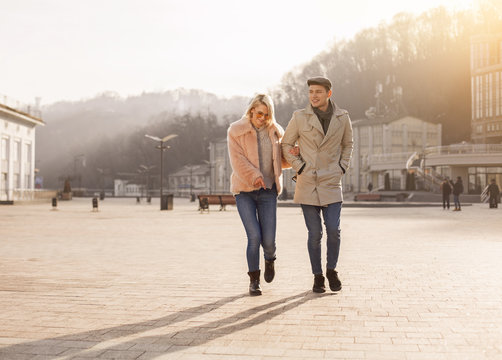 Look. Full length of happy young lovers are spending time outdoors while having cheerful mood. They are walking on square while girl in sunglasses is pointing finger on something down. Copy space