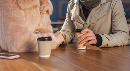 Tenderness of touch. Close up of hands of young pleasant couple on date is sitting at table and enjoying fresh espresso in open air