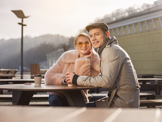 Nice time together. Portrait of cheerful relaxed smiling couple is sitting at table and drinking coffee while resting outdoors. They are looking at camera with joy