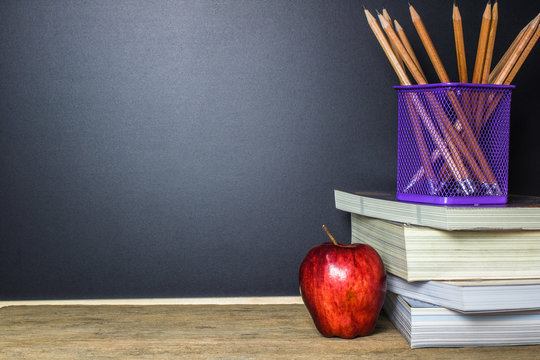 Education concept. Pencil and red apple on wood table with blackboard (chalkboard) as background with copy space.
