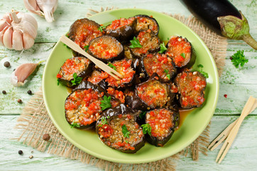 Eggplant slices in a spicy red sauce on the plate on wooden table